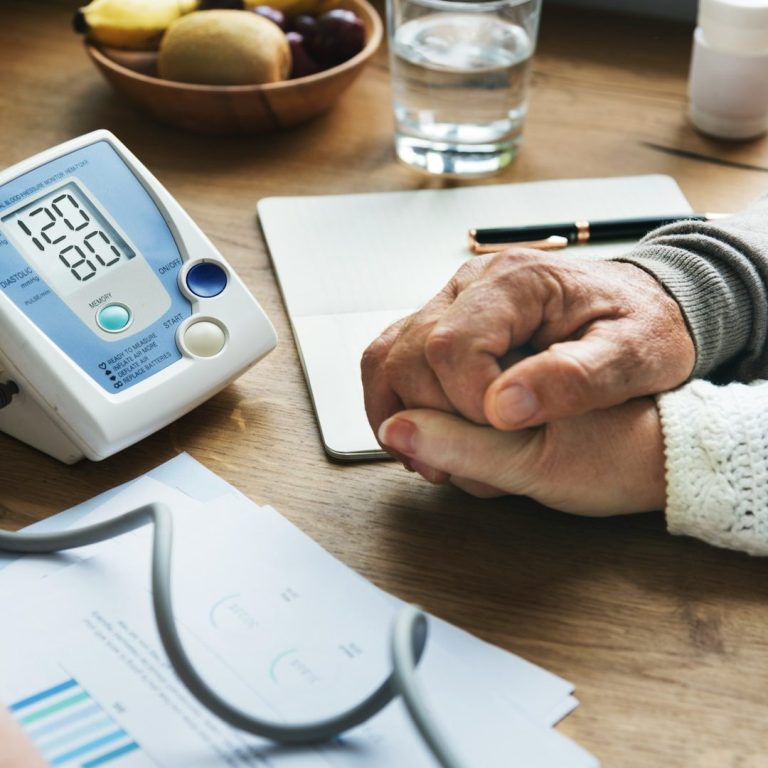 Bild von IONOS Hände greifen sich über einen Tisch mit Blutdruckmessgerät und Unterlagen.