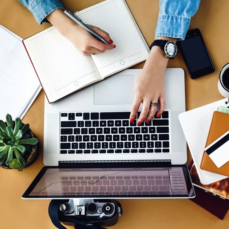 Bild von IONOS Ein Schreibtisch mit Laptop, Notizbuch, Tasse Kaffee und Pflanzen.