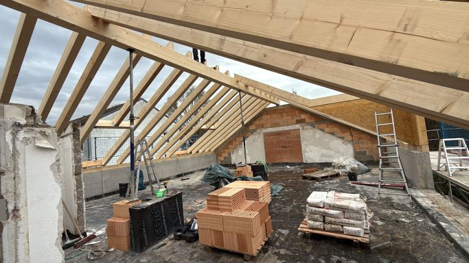 Dachbaumaterialien auf einer Baustelle mit unvollständiger Dachkonstruktion.