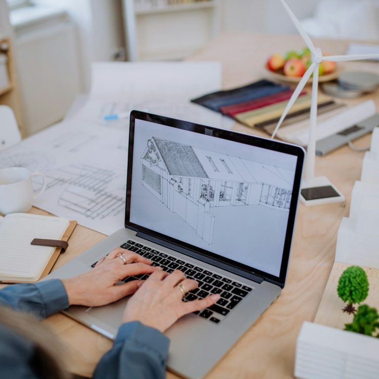 Bild von IONOS Person arbeitet an Laptop mit Entwürfen und Materialien auf dem Tisch.