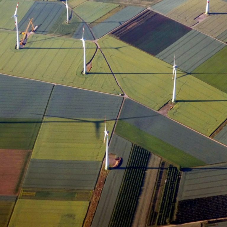 Bild von IONOS Luftaufnahme von Feldern mit Windkraftanlagen und abwechslungsreicher grüner Landschaft.