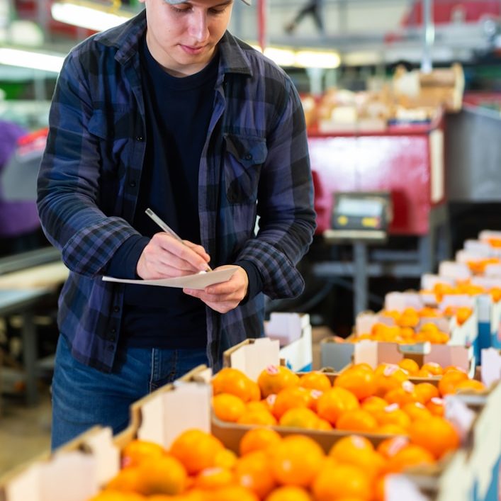 Mann schreibt an einem Tisch mit Kisten voller Orangen.