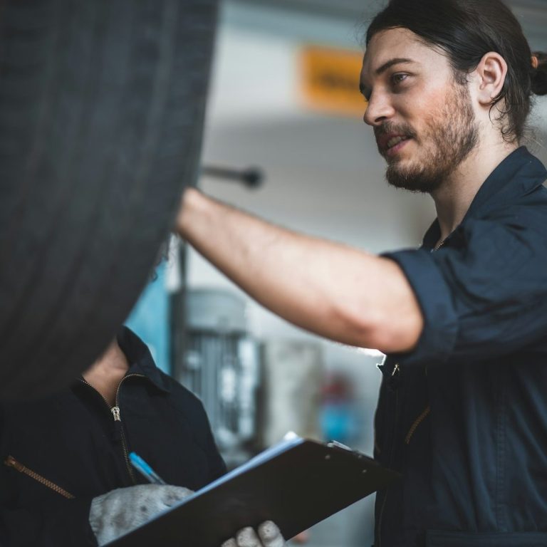 Mechaniker überprüft Reifen und hält dabei einen Klemmbrett in der Werkstatt.