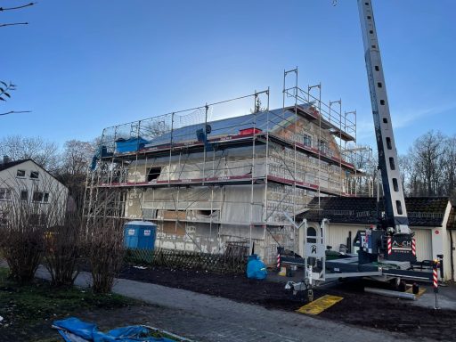 Neubau mit Gerüst, Kränen und Baustellenfahrzeugen in einer urbanen Umgebung.