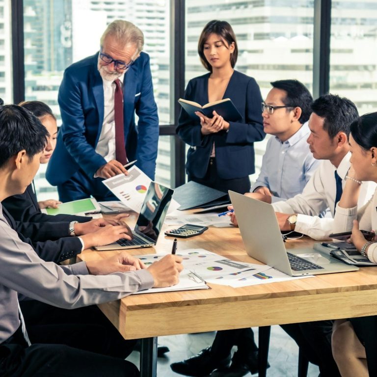 Bild von IONOS Gruppendiskussion in einem modernen Büro mit sieben Personen und Laptops auf dem Tisch.